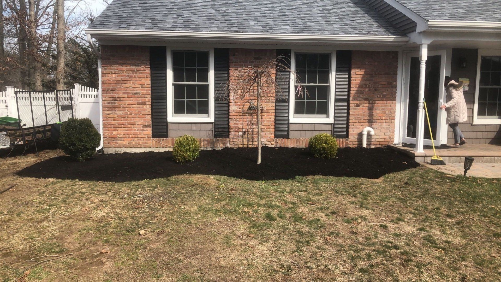 A man is standing in front of a brick house with black shutters.