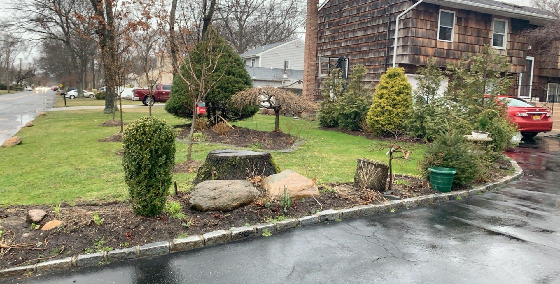 A red car is parked in front of a house on a rainy day.