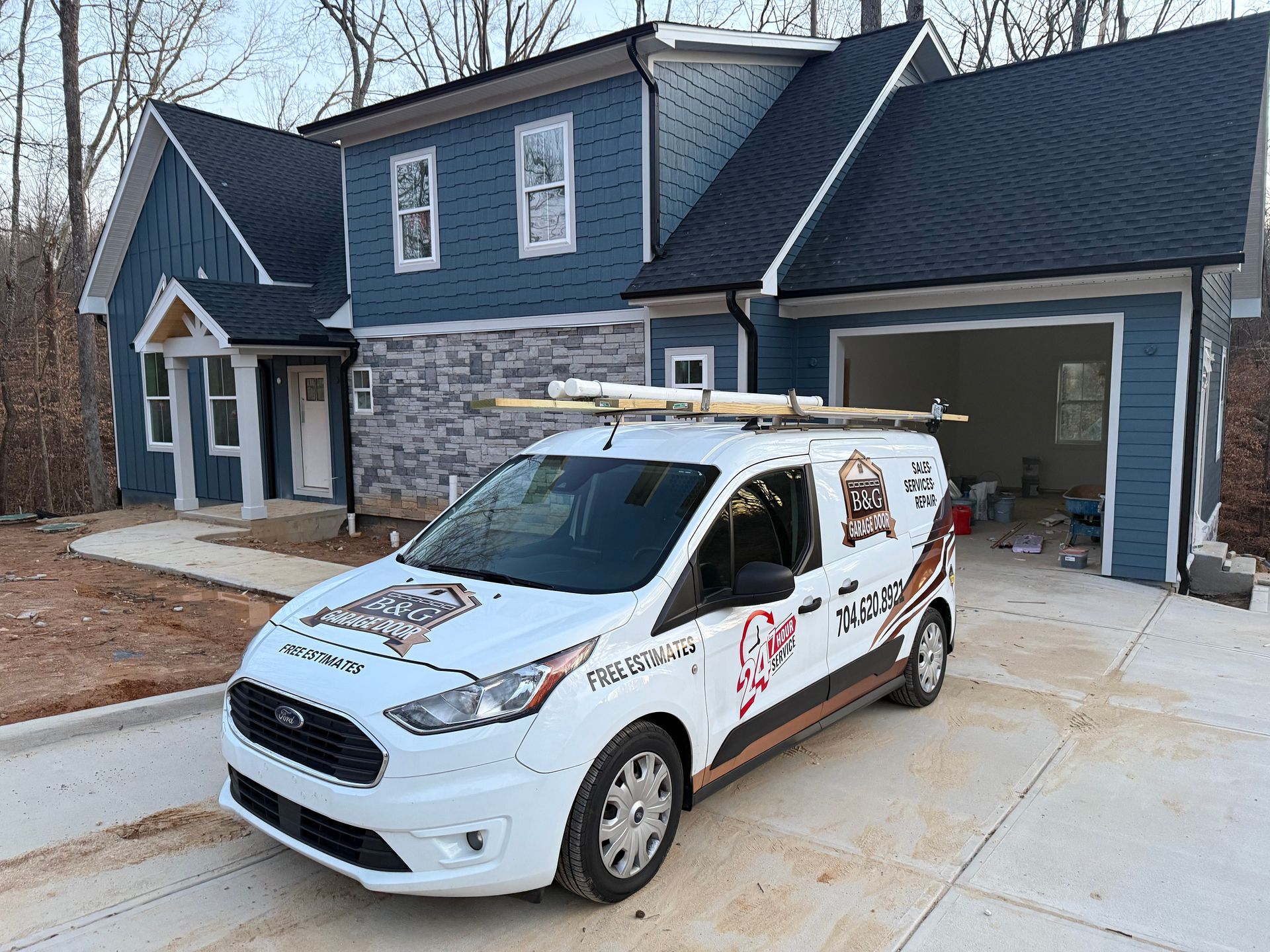 White service van parked in a driveway beside a blue-gray house with a stone facade