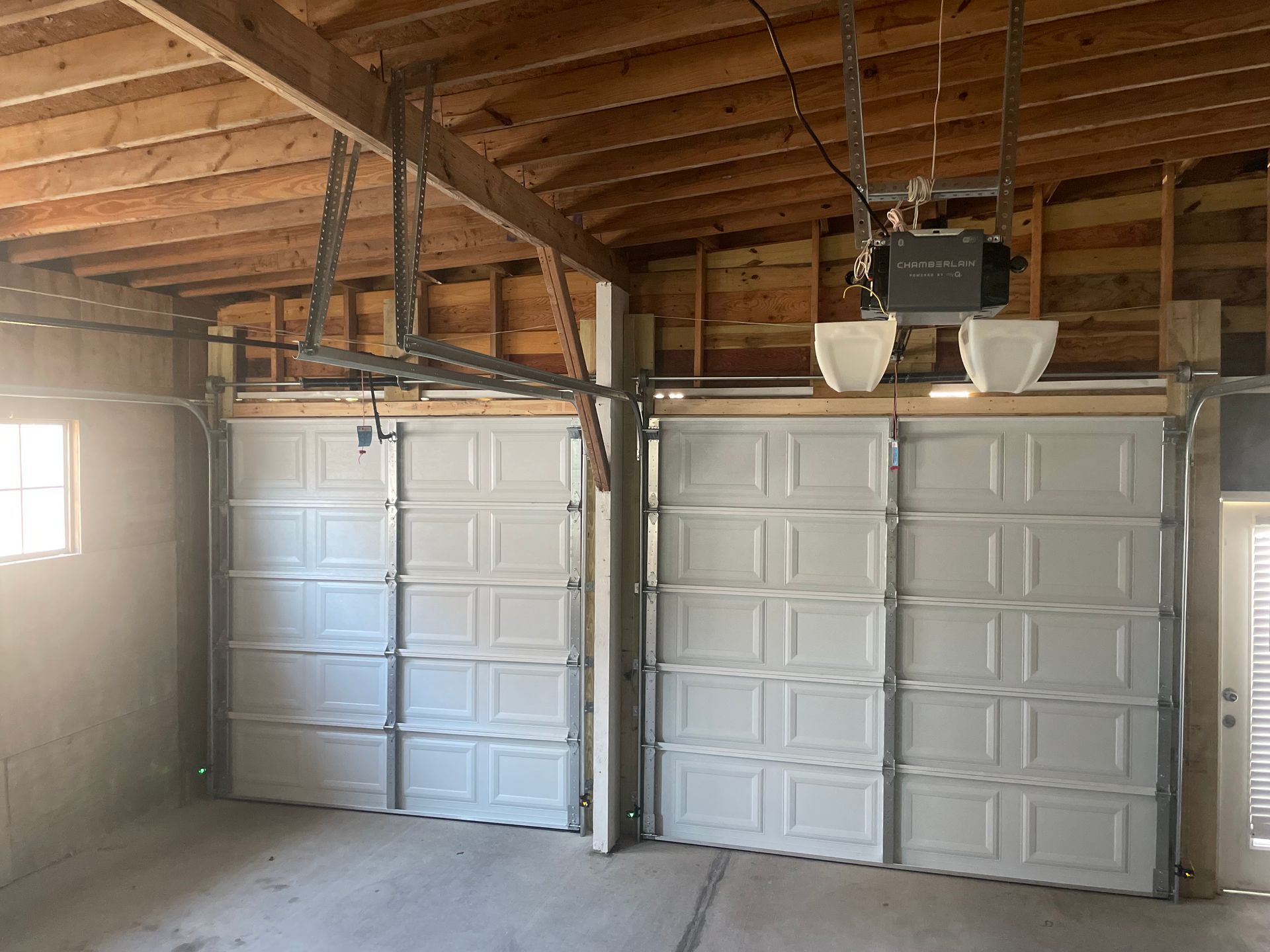 Interior of a garage with two white paneled garage doors and exposed wooden ceiling beams.