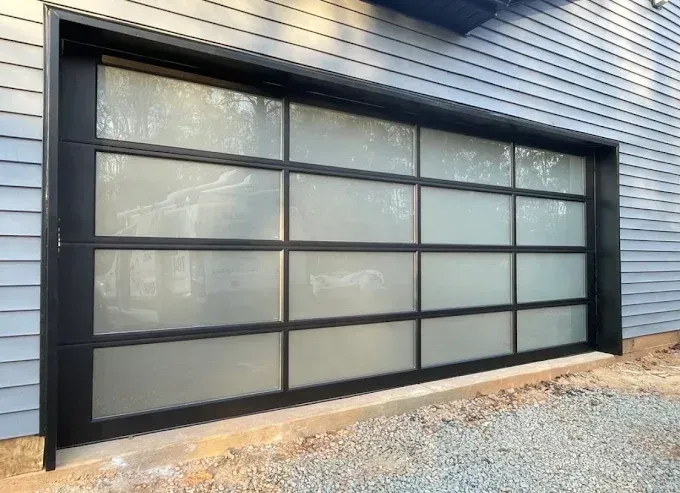 Modern frosted glass garage door with black frame on a blue house exterior