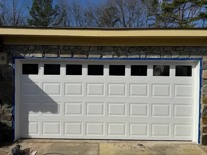 White garage door with four small windows, set in a stone house exterior under a roof overhang.