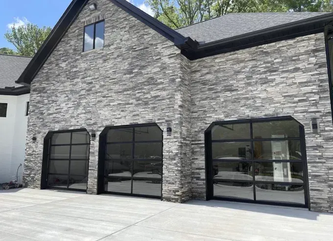 Modern stone house exterior with large black-framed windows and a concrete driveway