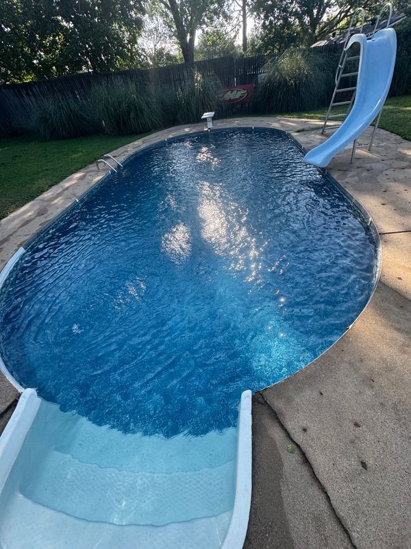 Man working on pool plumbing in a concrete enclosure next to a pool.