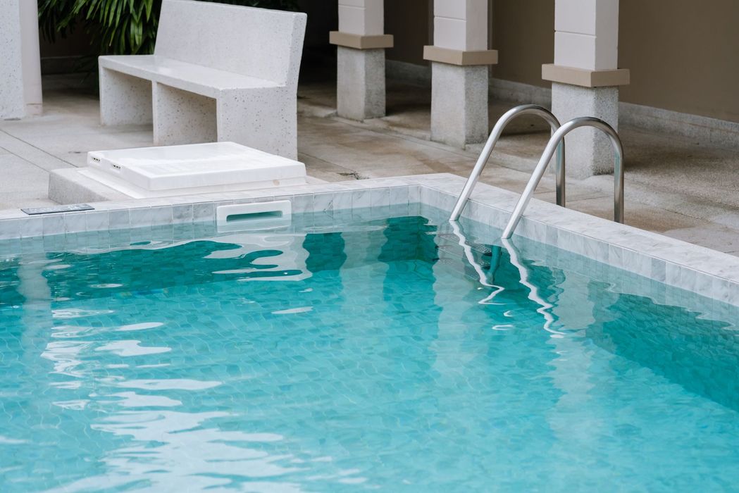 Swimming pool with turquoise water, a ladder, and a concrete bench in an outdoor setting.