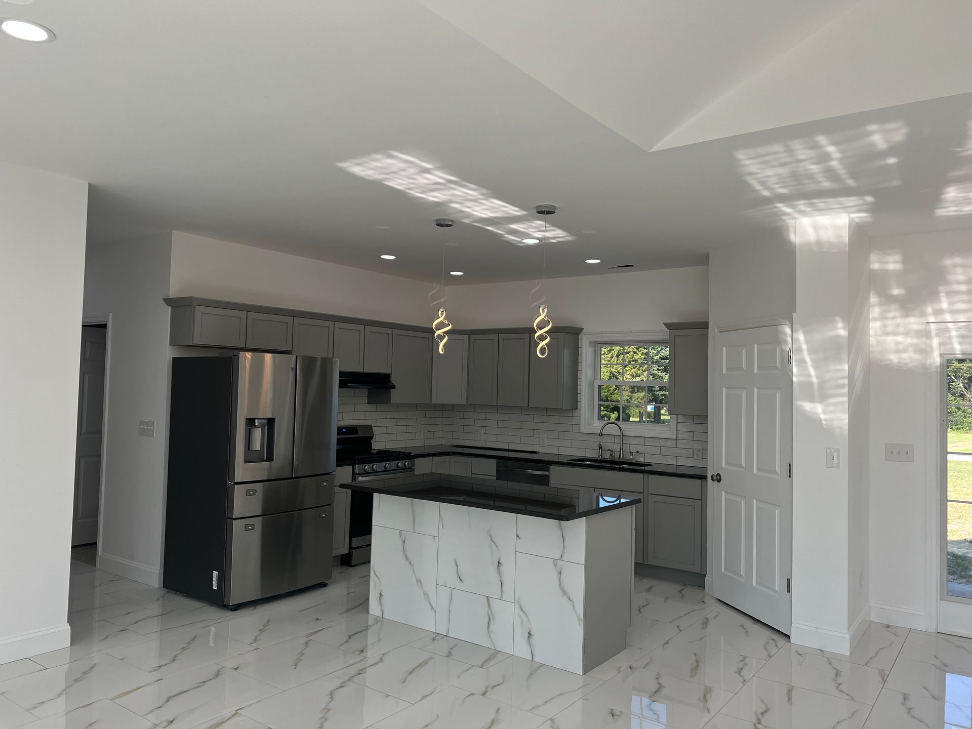 Modern kitchen with gray cabinets, marble-patterned island, stainless refrigerator, and white tile floors
