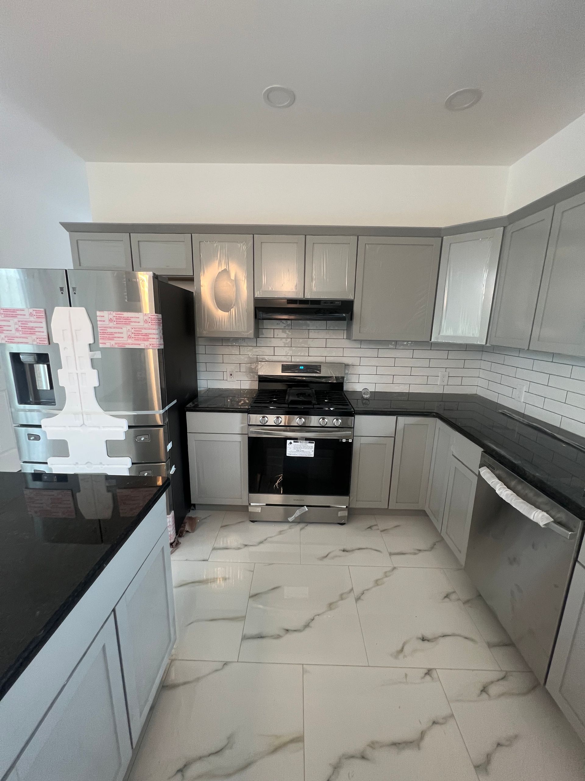 Modern gray kitchen with stainless steel appliances, marble-look floor, and white backsplash tiles