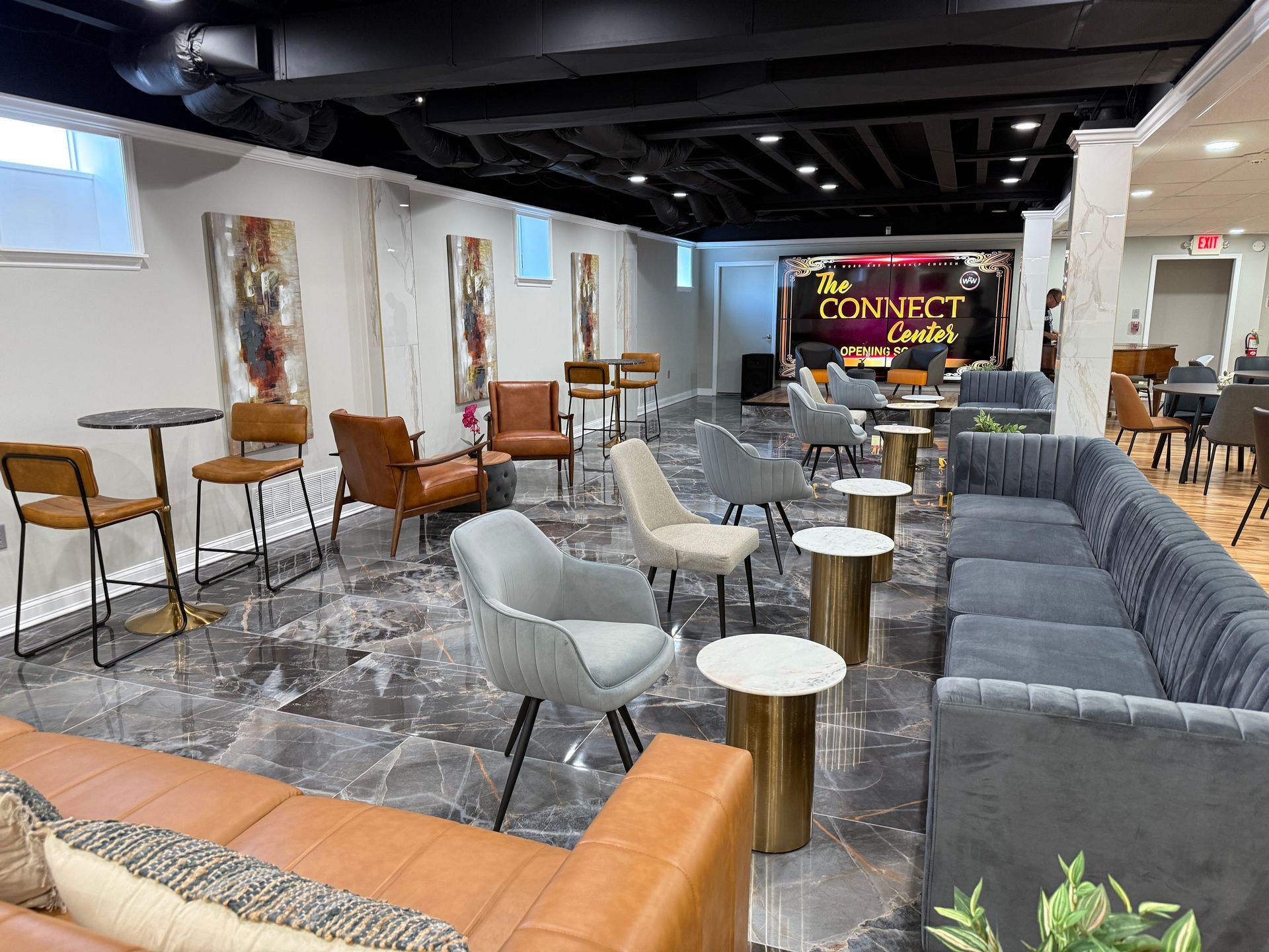 A modern event space with neutral decor, featuring leather and gray armchairs, cocktail tables, and marble-look flooring