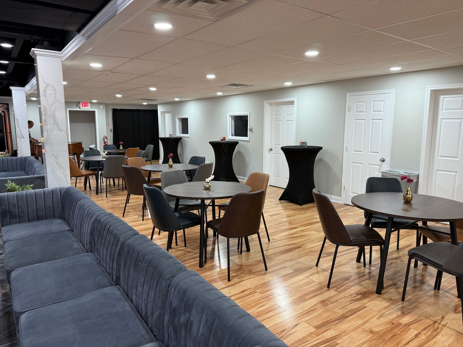 Empty event hall with round tables, black chair covers, and a gray sectional sofa on wood flooring