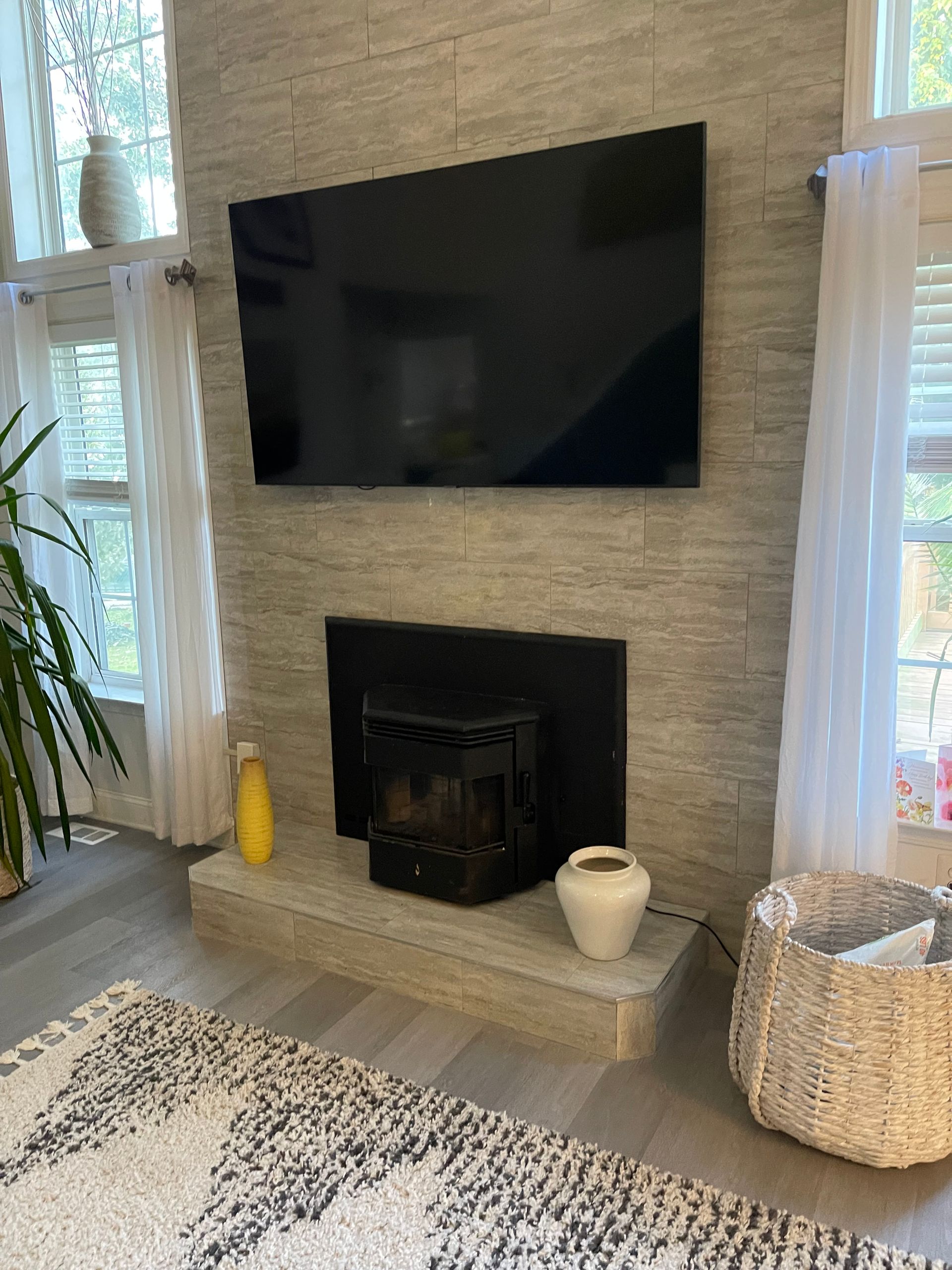 Modern living room fireplace with a wall-mounted TV, light stone surround, and tall windows with white curtains