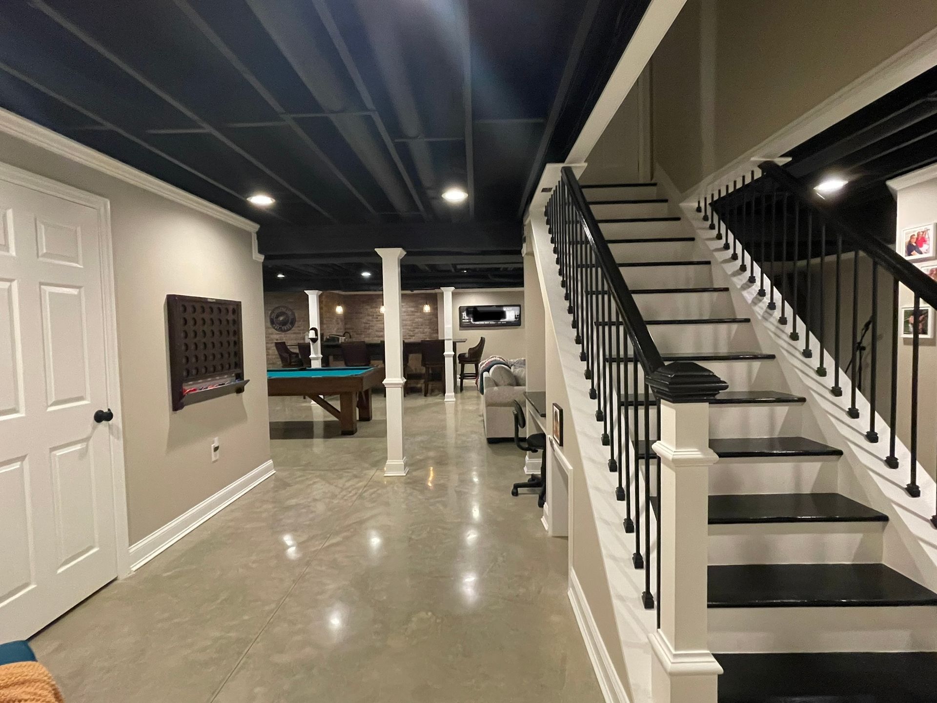 Basement with a staircase featuring black treads and white railings, a concrete floor, and a pool table in the background