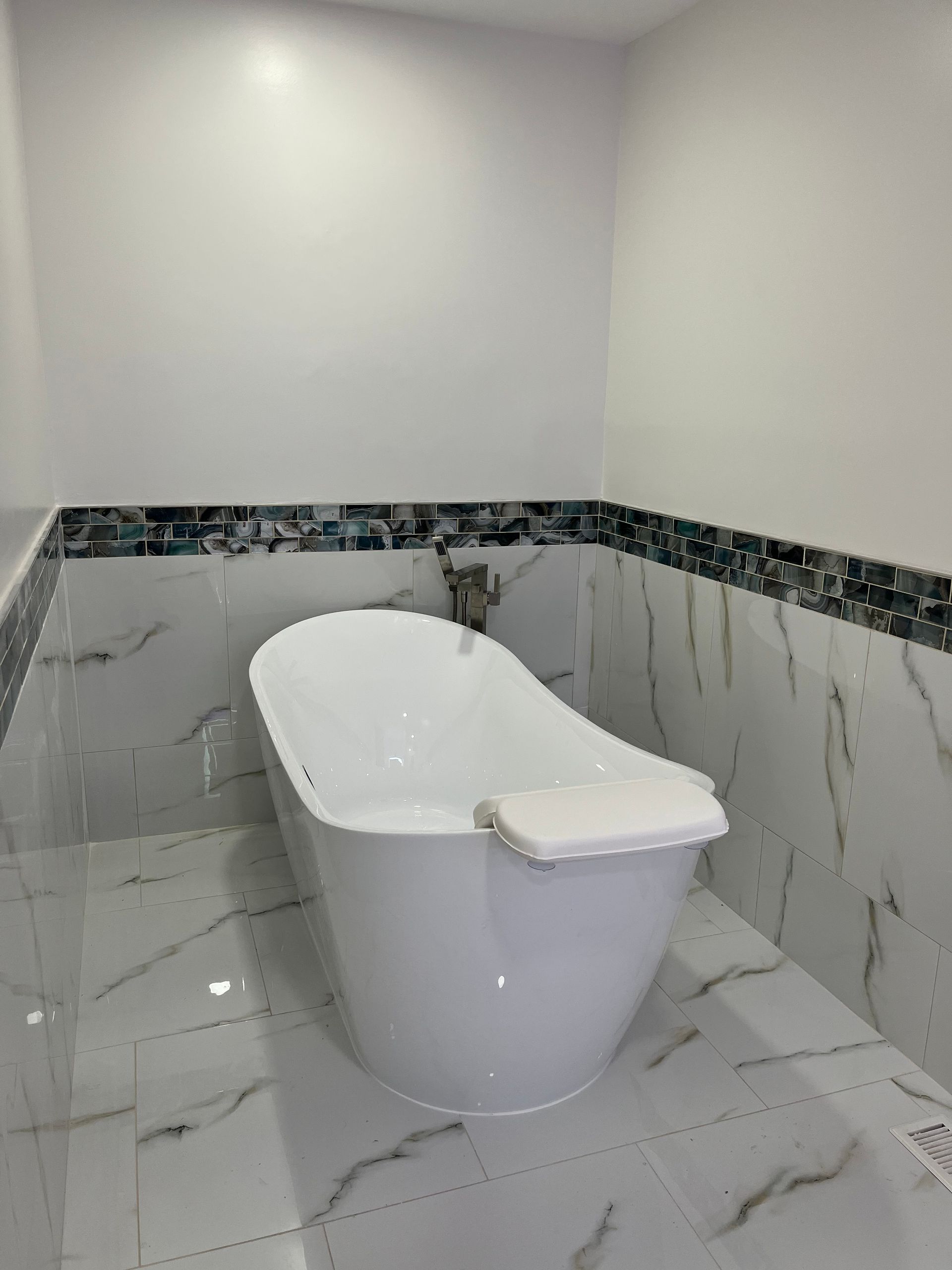 White freestanding bathtub in a tiled bathroom with gray marble floor and wall accents