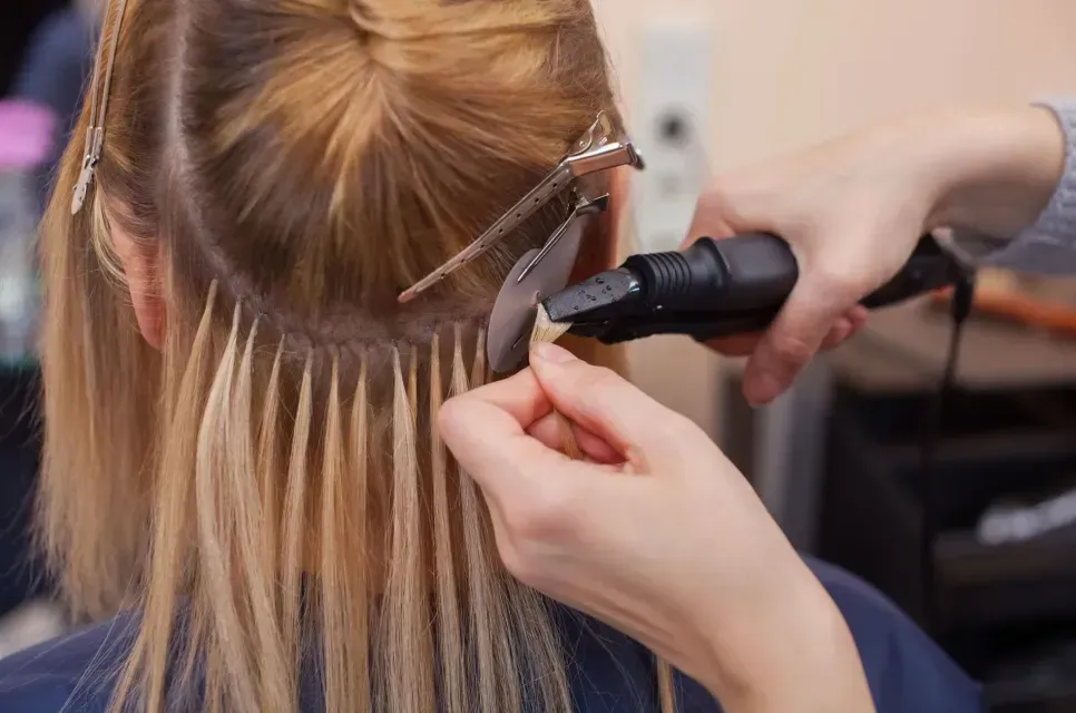 Stylist using a curling iron to style blonde hair with hair clips in a salon