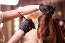 Gloved hands applying hair dye to a client’s brown hair in a salon