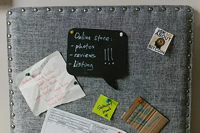 Cork board with sticky notes and small signs, including a black note listing online store tasks.