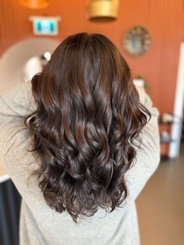 Back view of long, wavy dark brown hair in a softly lit salon setting