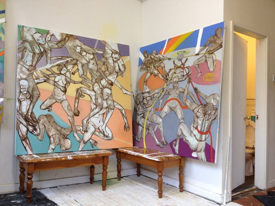 Two large paintings of figures, displayed on easels in a corner of a studio, colorful geometric backgrounds.