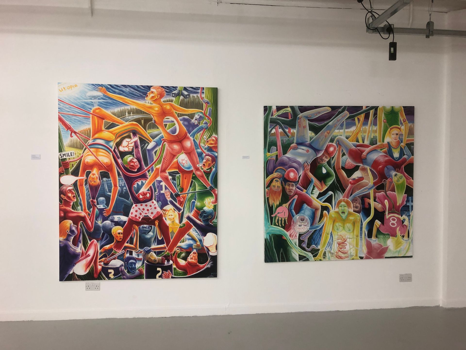 Two large, vibrant paintings on a white gallery wall. Figures in dynamic poses, colorful chaos.