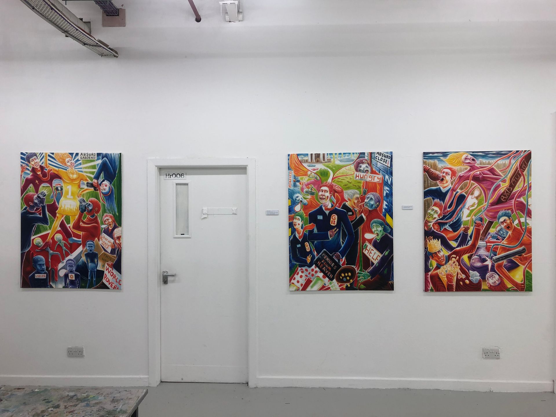 Three colorful paintings displayed on a white wall in a gallery setting, alongside a closed white door.