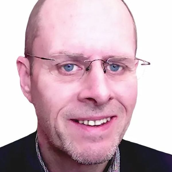 john hogan with glasses smiling, blue eyes, fair skin, close-up, black jacket, white background.