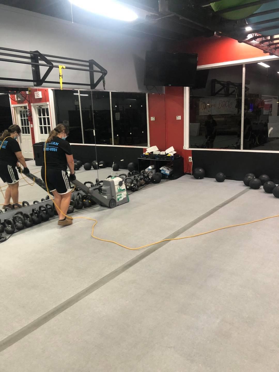 A woman is cleaning a gym floor with a vacuum cleaner.