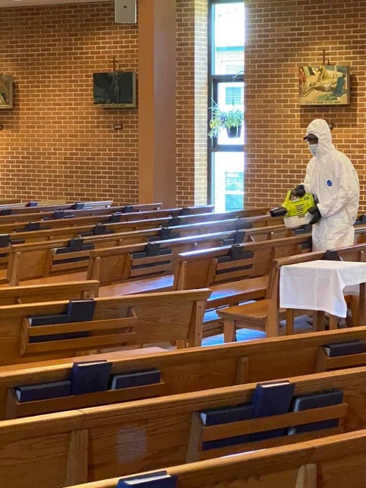 A man in a protective suit is disinfecting a church with a sprayer.