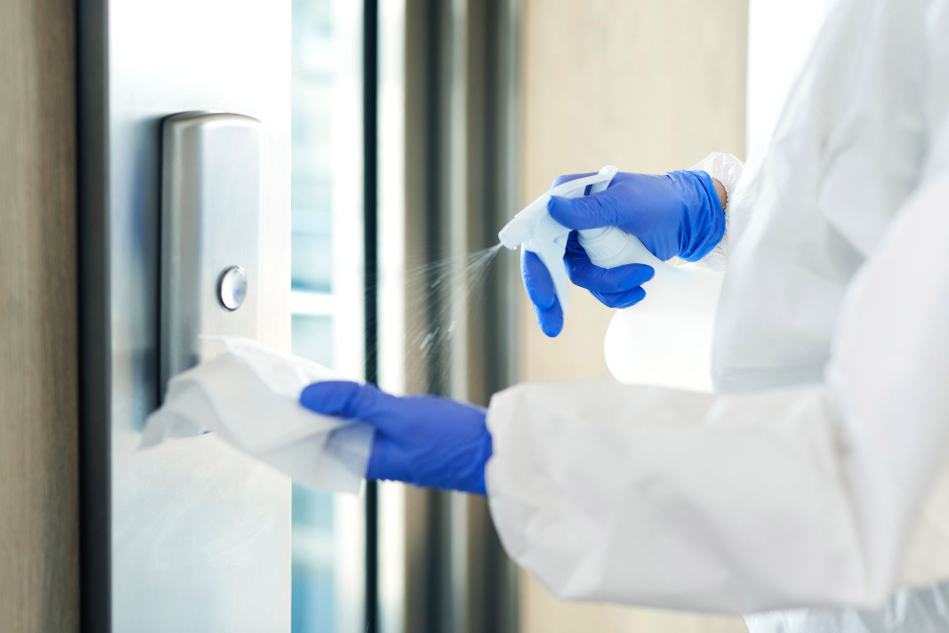A person wearing blue gloves is cleaning a door with a spray bottle