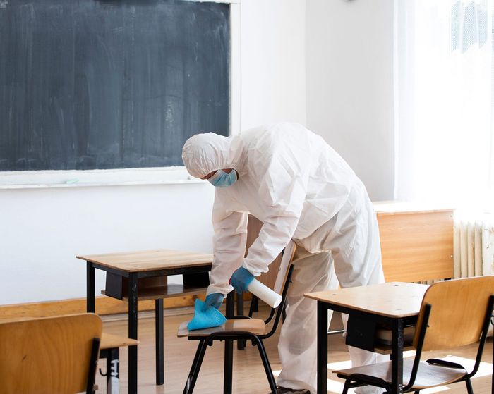 A man in a protective suit is spraying a room with a sprayer.