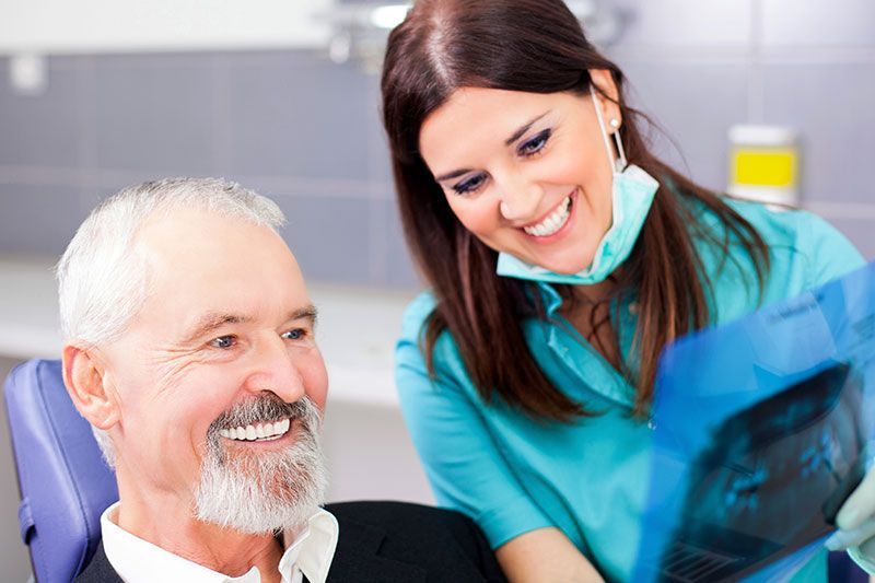 A dentist is looking at an x-ray of a man 's teeth.