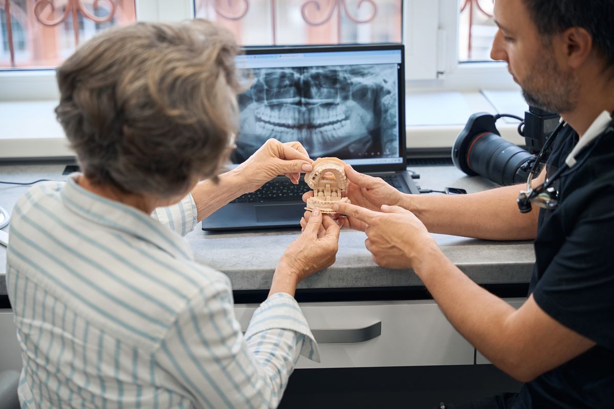 Dentist showing a dental model to a patient beside an X-ray on a monitor