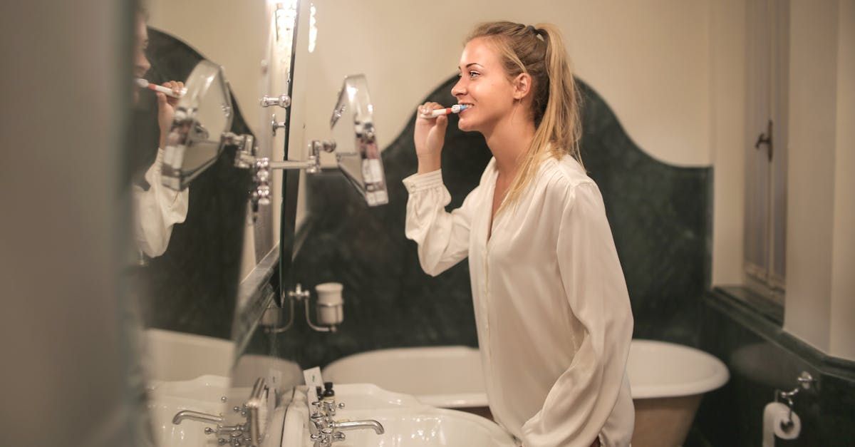 A woman is brushing her teeth in front of a bathroom mirror.