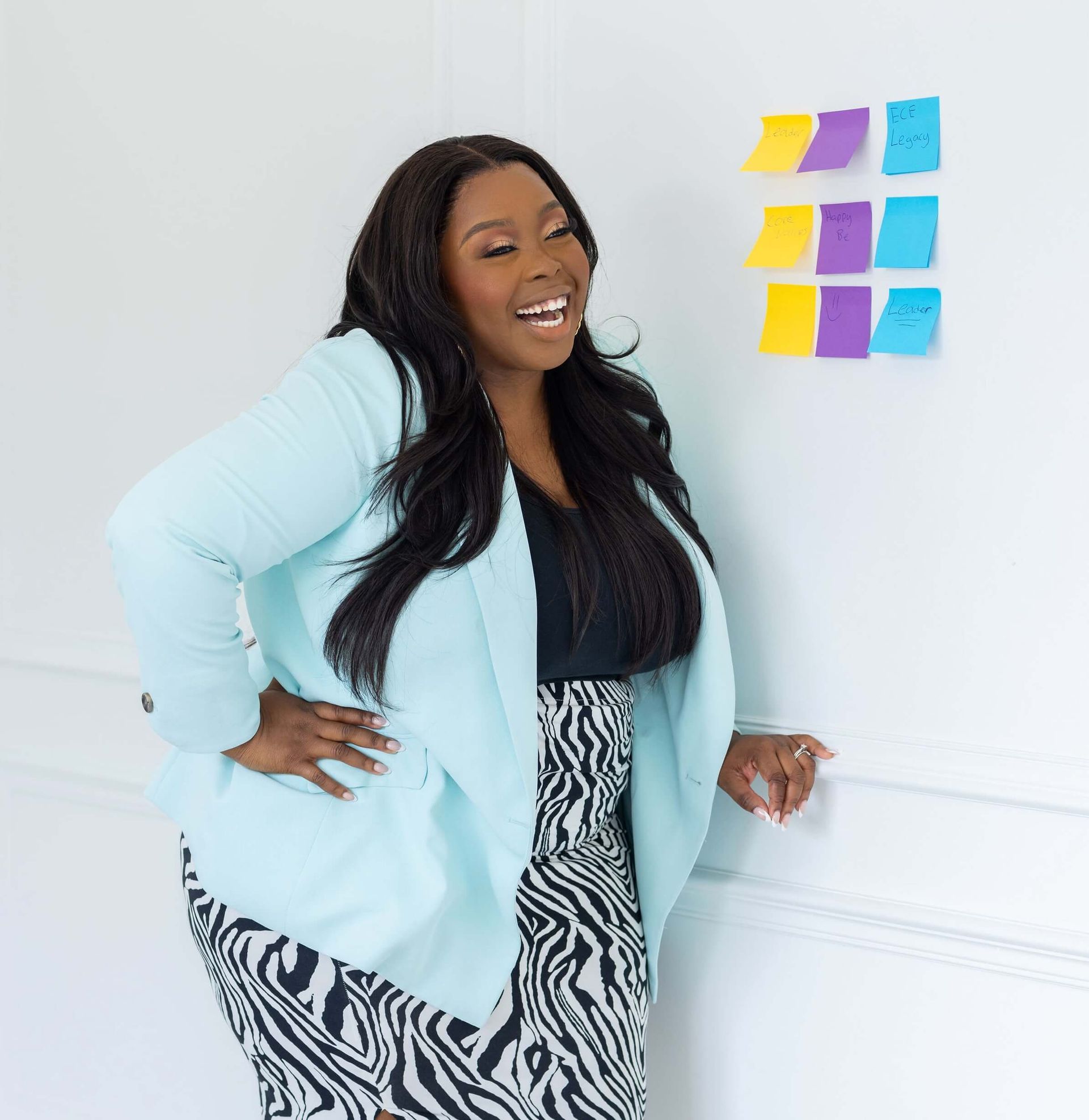 Anisha Angella, the Early Childhood Coach, smiling against a wall with post-it notes on it