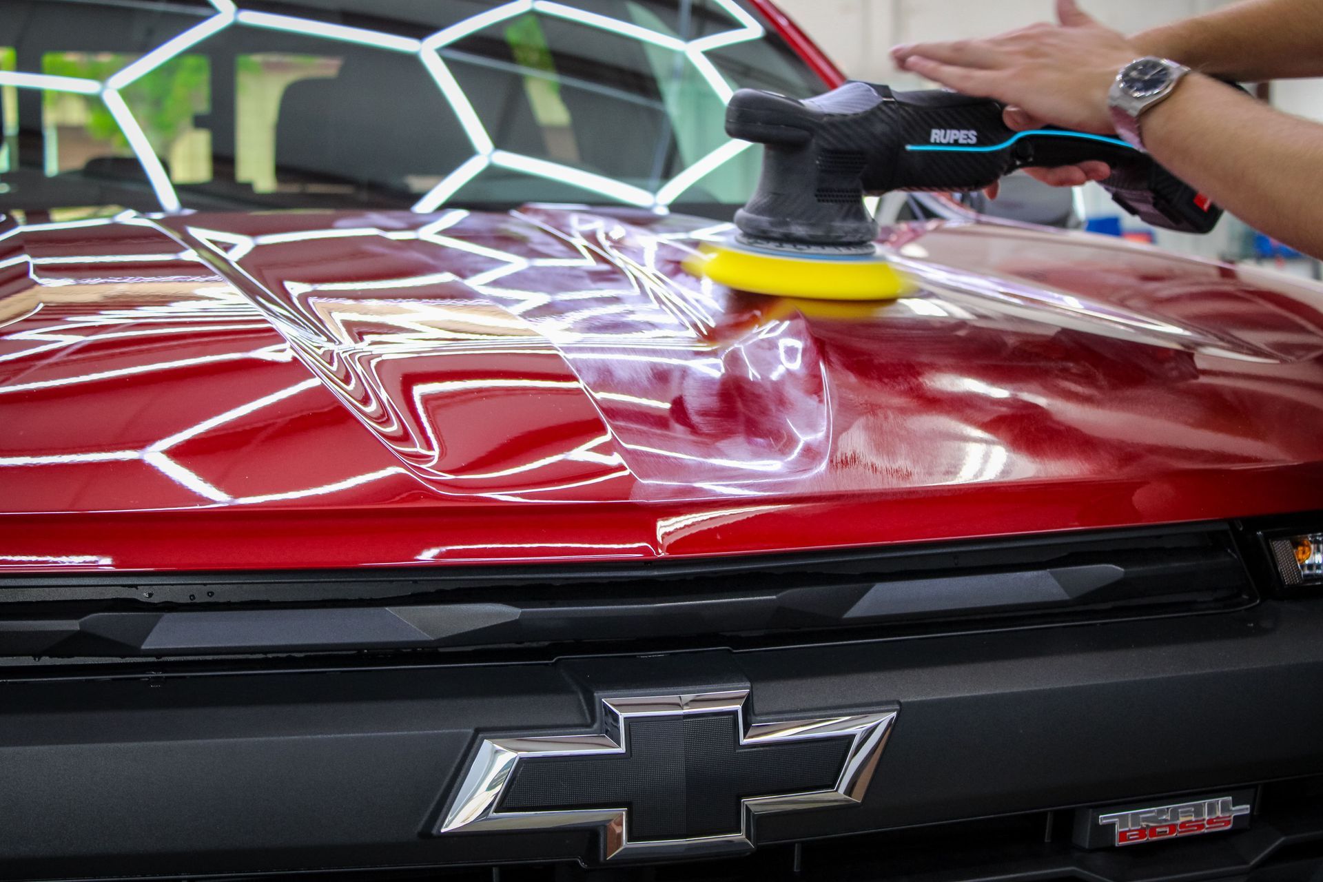 Person using a polisher on a red Chevrolet truck hood.