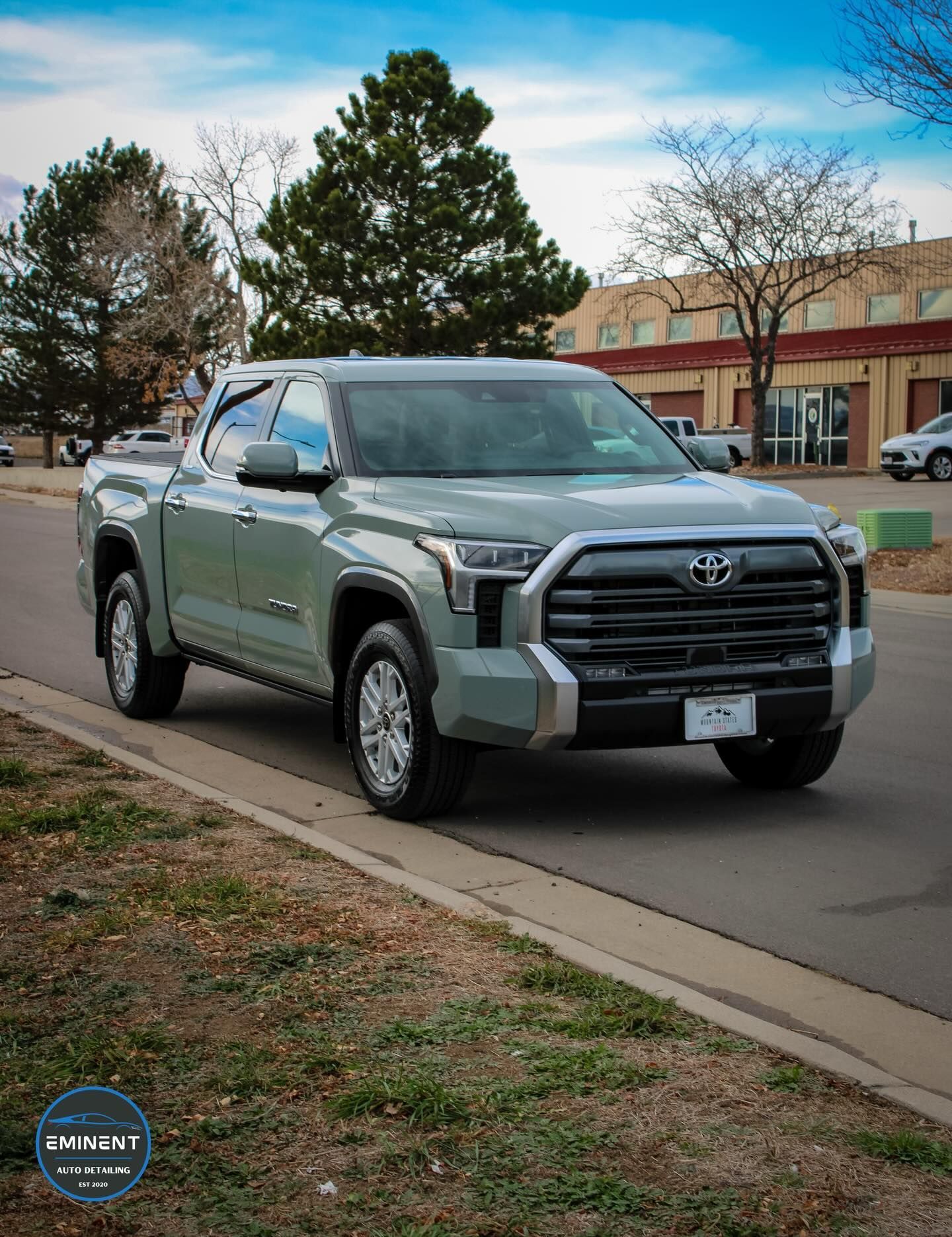 Green Toyota Tundra pickup truck parked on a street in front of a building on a partly cloudy day.