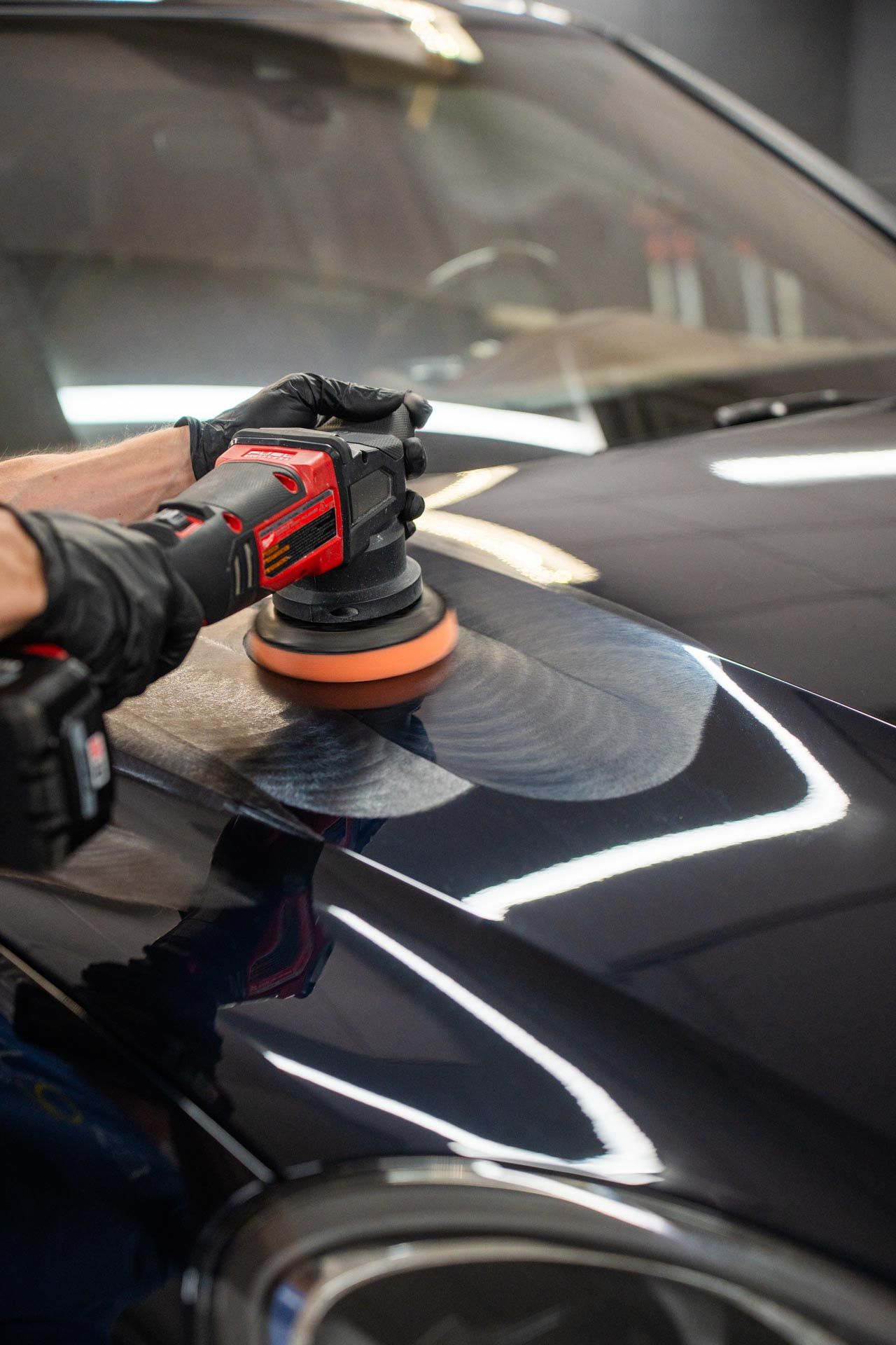 Man applying film to white truck hood in a shop. Fluorescent lights and tools visible.