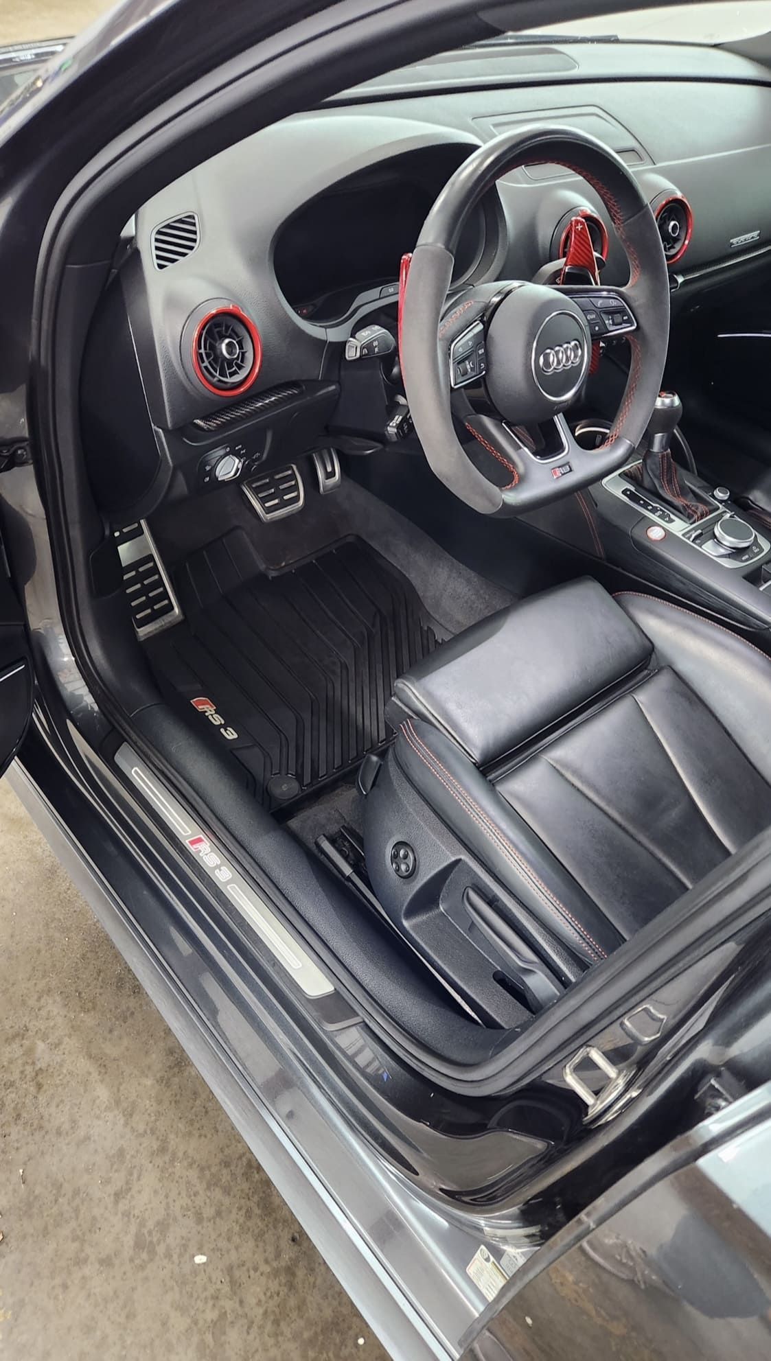 Interior of a black Audi RS3. Black leather seats, steering wheel with red accents. Rubber floor mats.