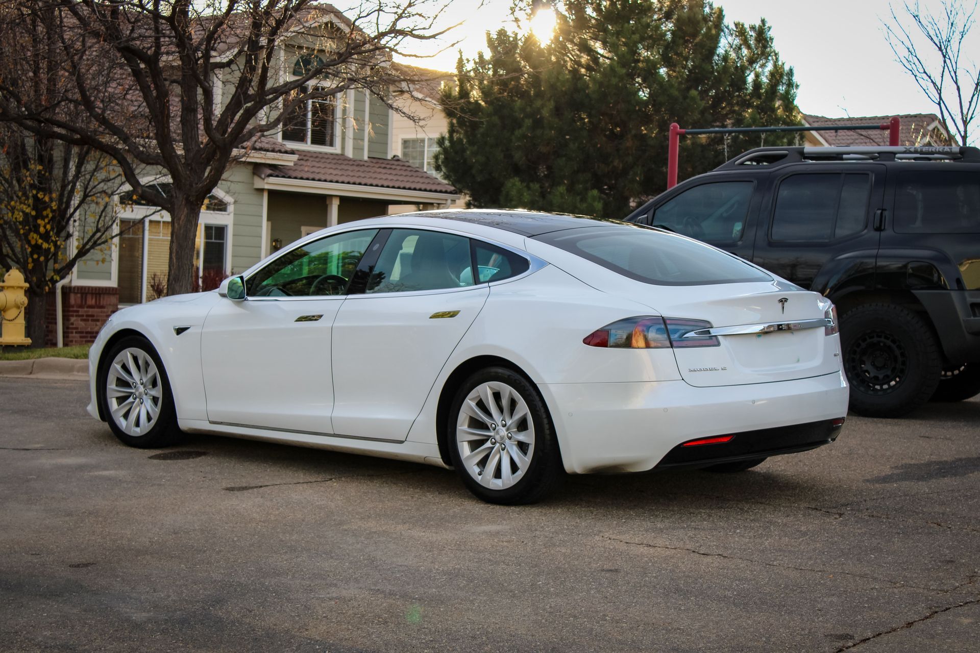 White Tesla sedan parked on a street near a house.