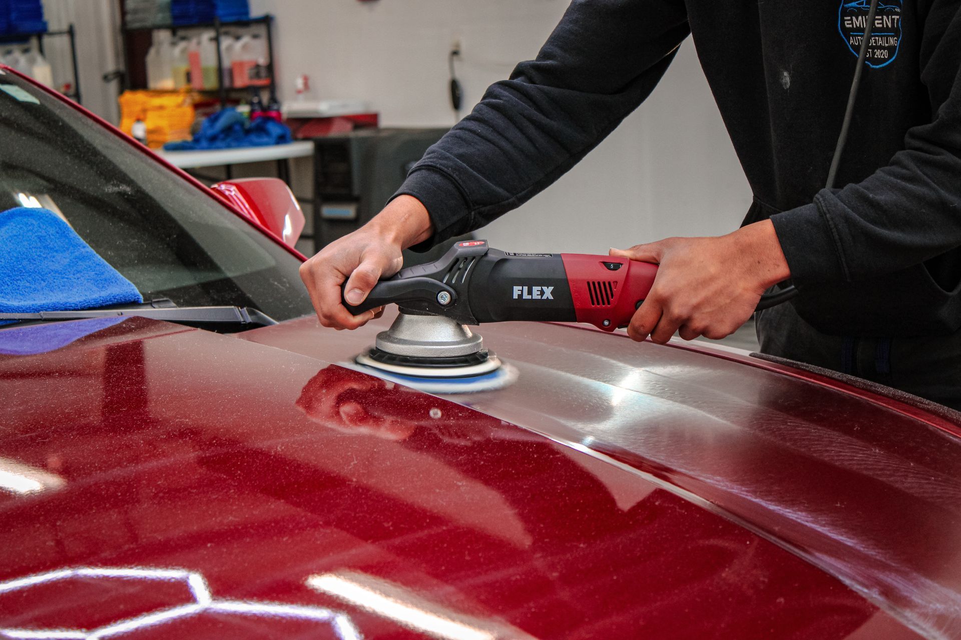 Person polishes a red car hood with a power buffer in a workshop, removing imperfections.