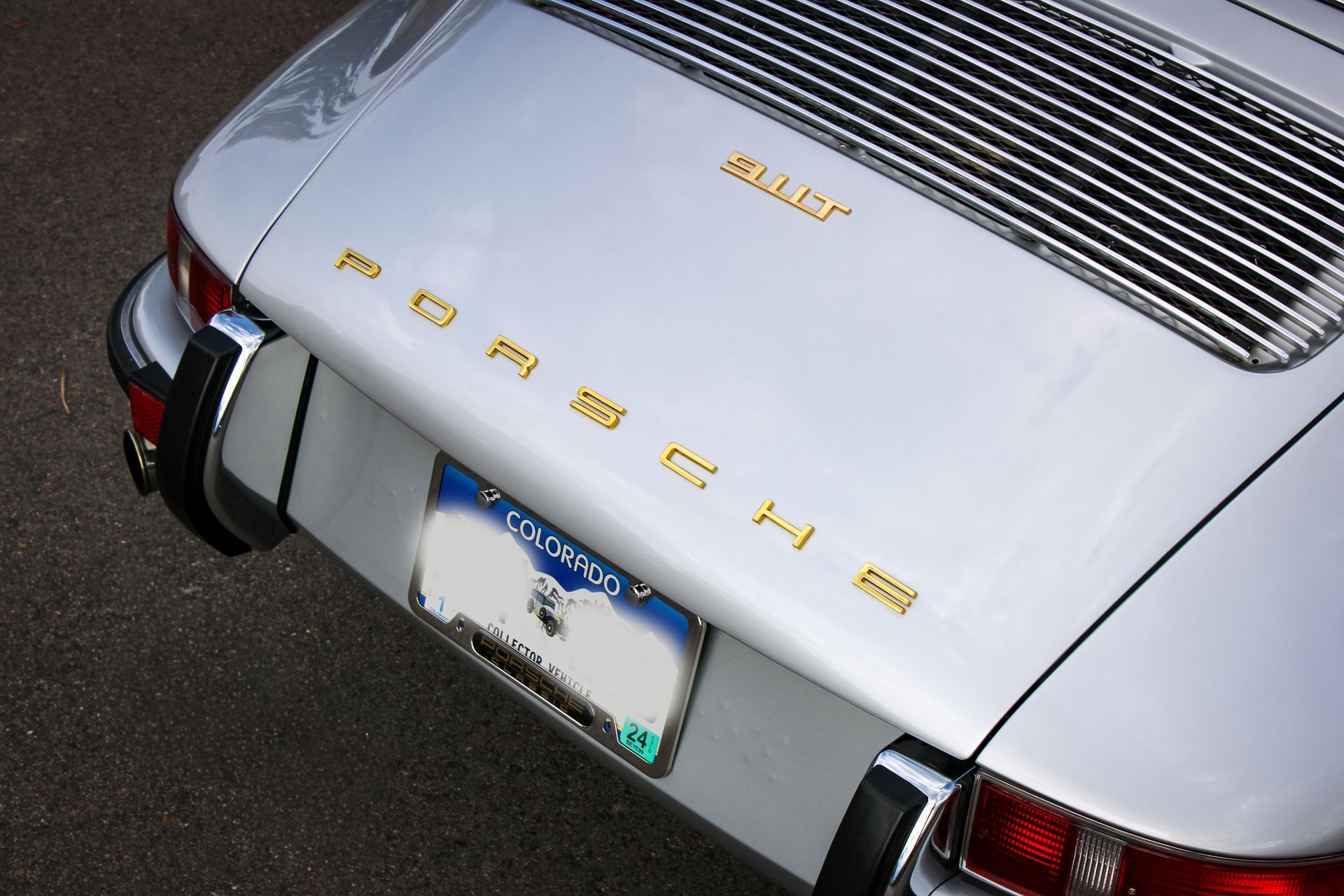 Three people applying protective film to the hood of a white SUV in a workshop. One sprays water.