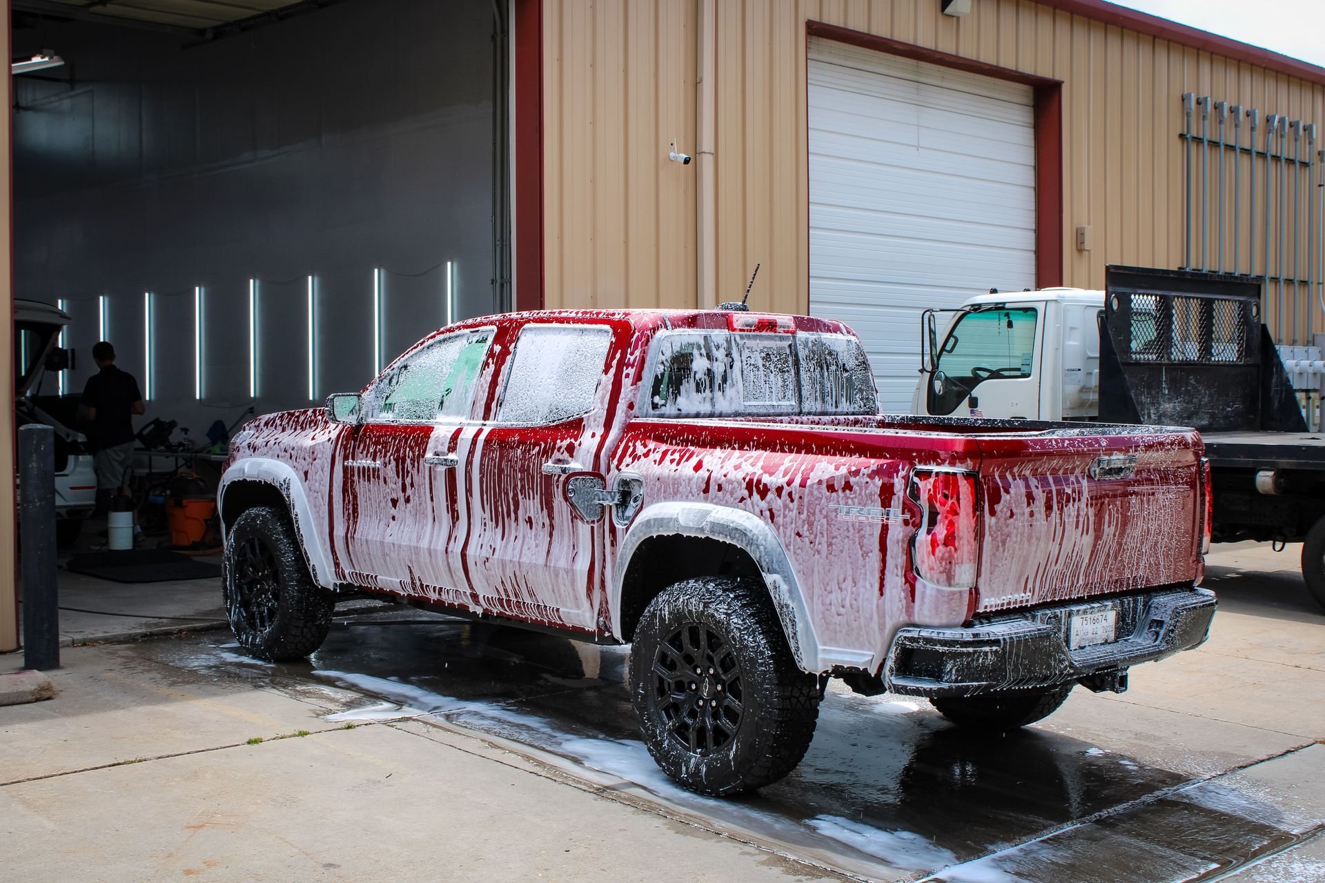 Red pickup truck covered in soap suds, outside a building with garage doors.