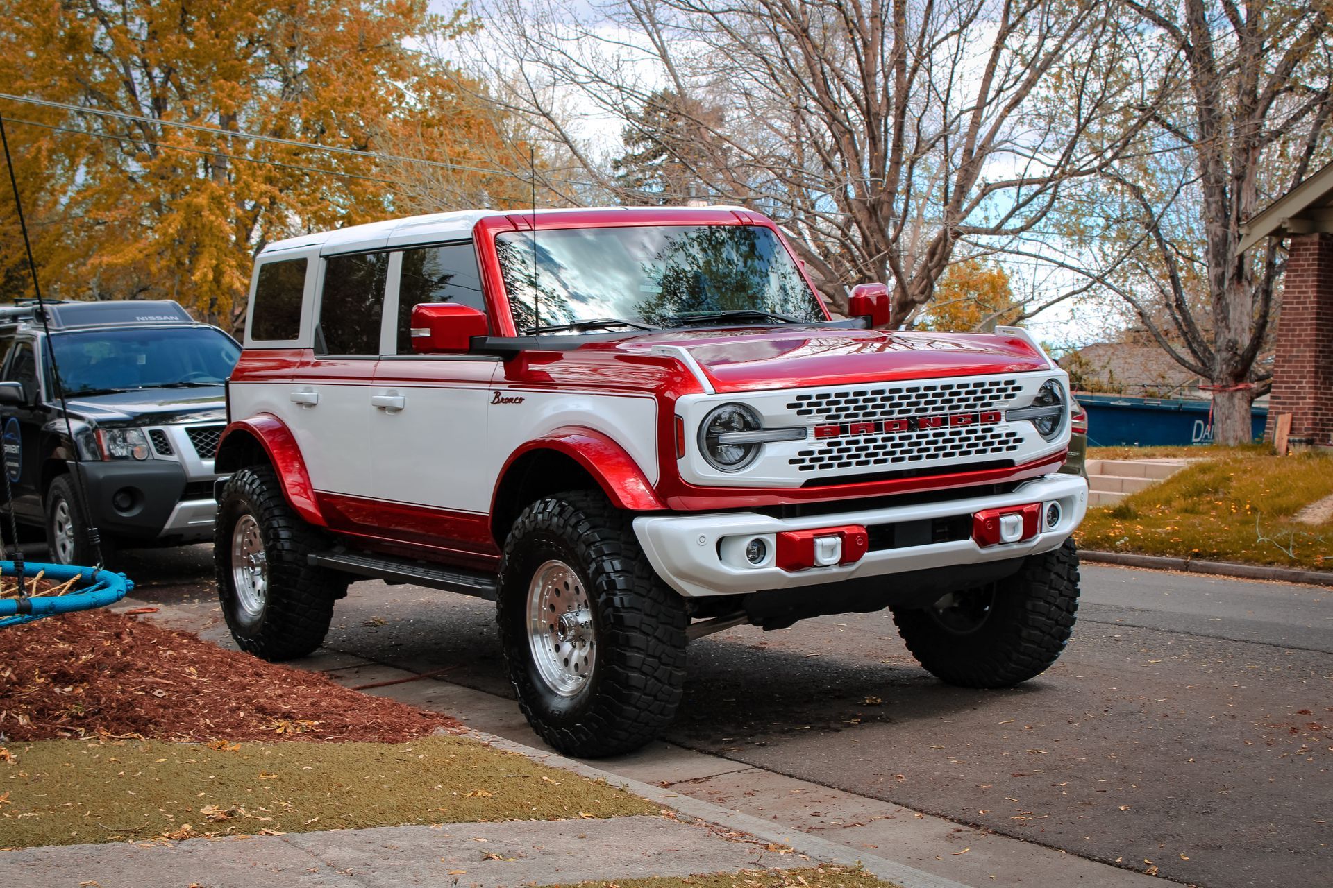 Red and white Ford Bronco parked on a residential street with trees.