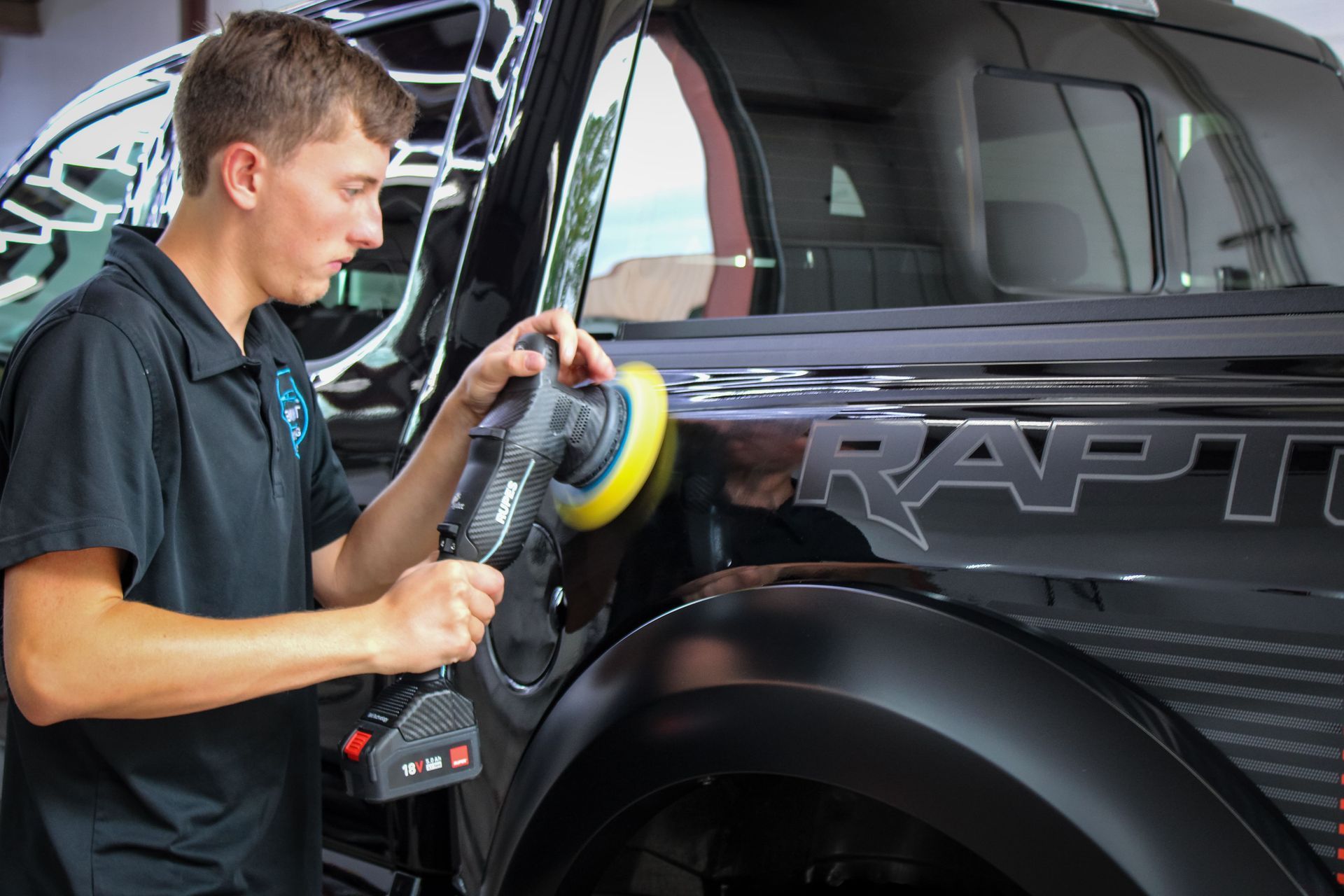 Man polishing a black truck with a power tool.