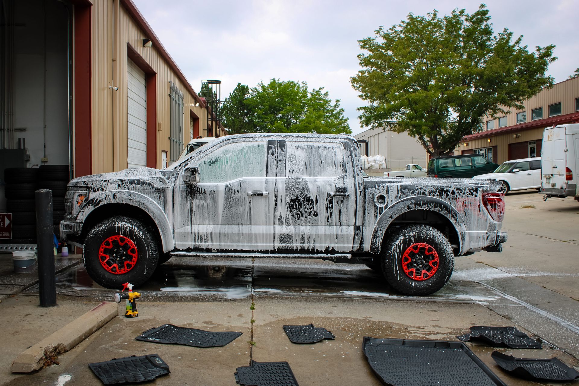 White pickup truck covered in soap, being washed outside a garage. Black floor mats on ground.