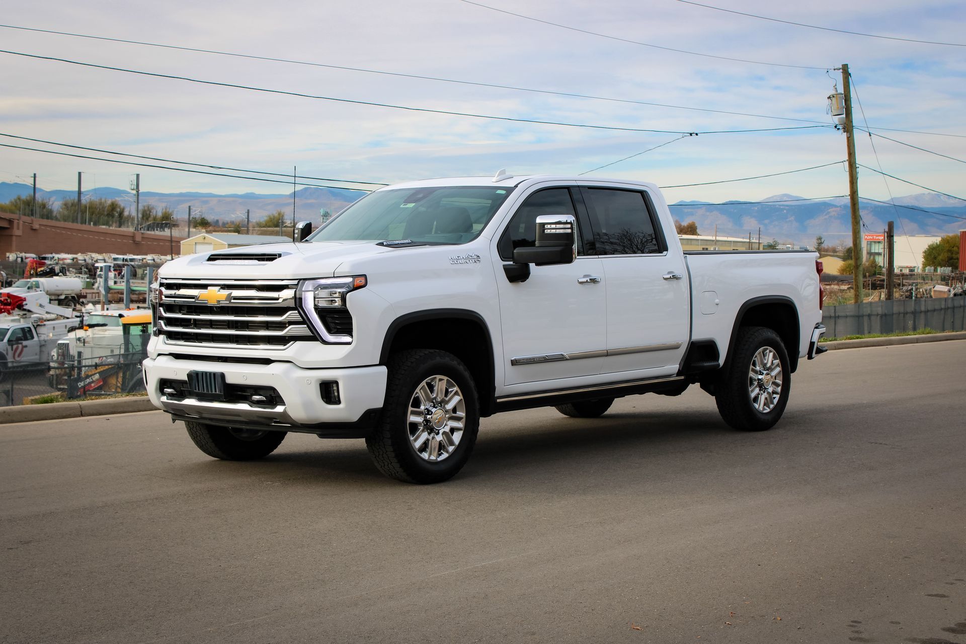 White Chevrolet pickup truck parked on an asphalt road with a building and mountains in the background.