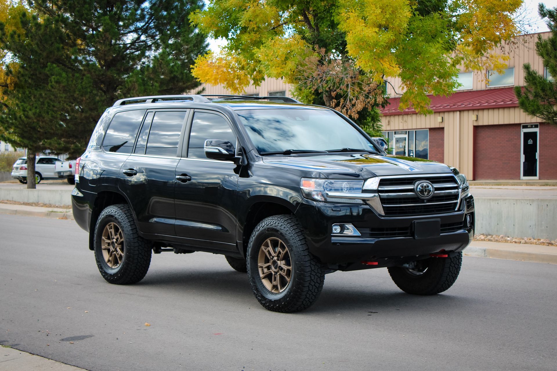 Black Toyota Land Cruiser SUV with bronze wheels parked on a street in front of a building.