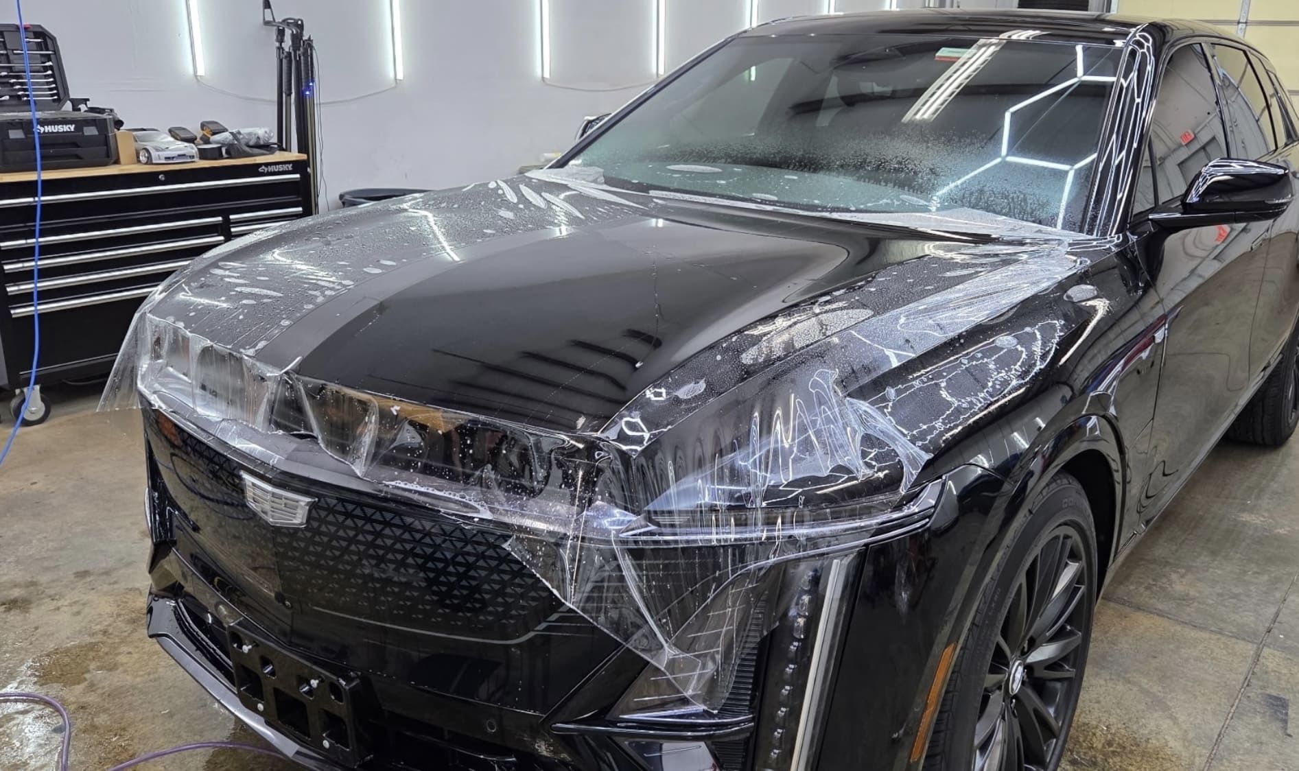 Black SUV with clear protective film on hood and headlights in a garage.