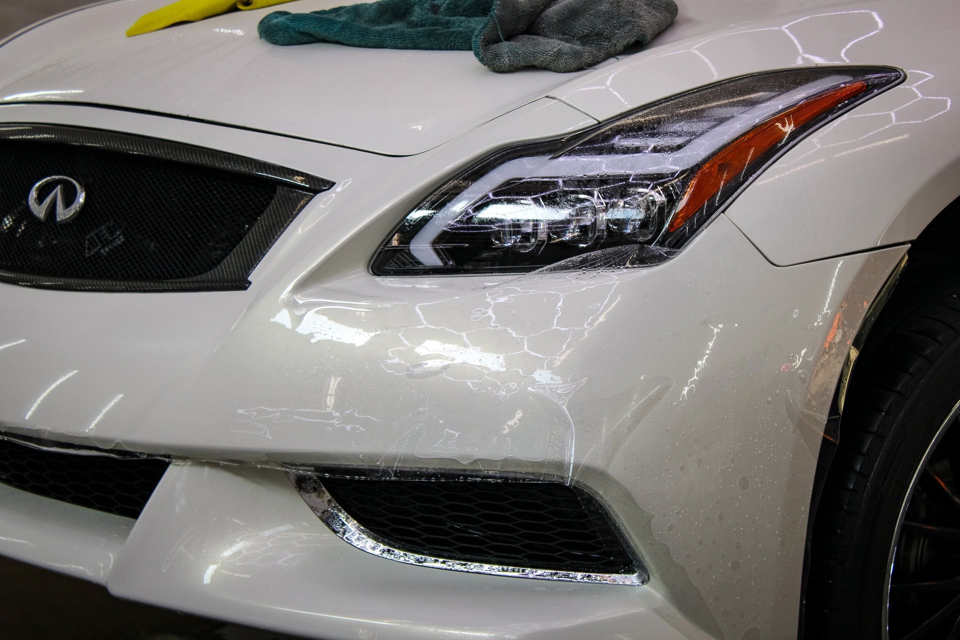 White Infiniti car front end close-up, with grill and headlight detail, being cleaned.