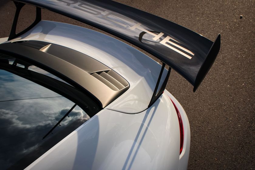 White Porsche sports car with a large carbon fiber spoiler on asphalt.