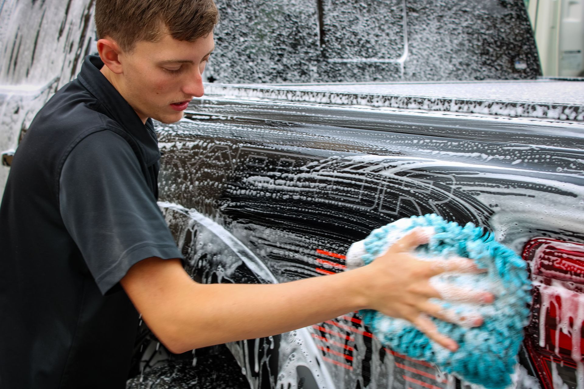 Person washing a red vehicle with a soapy sponge at a car wash.