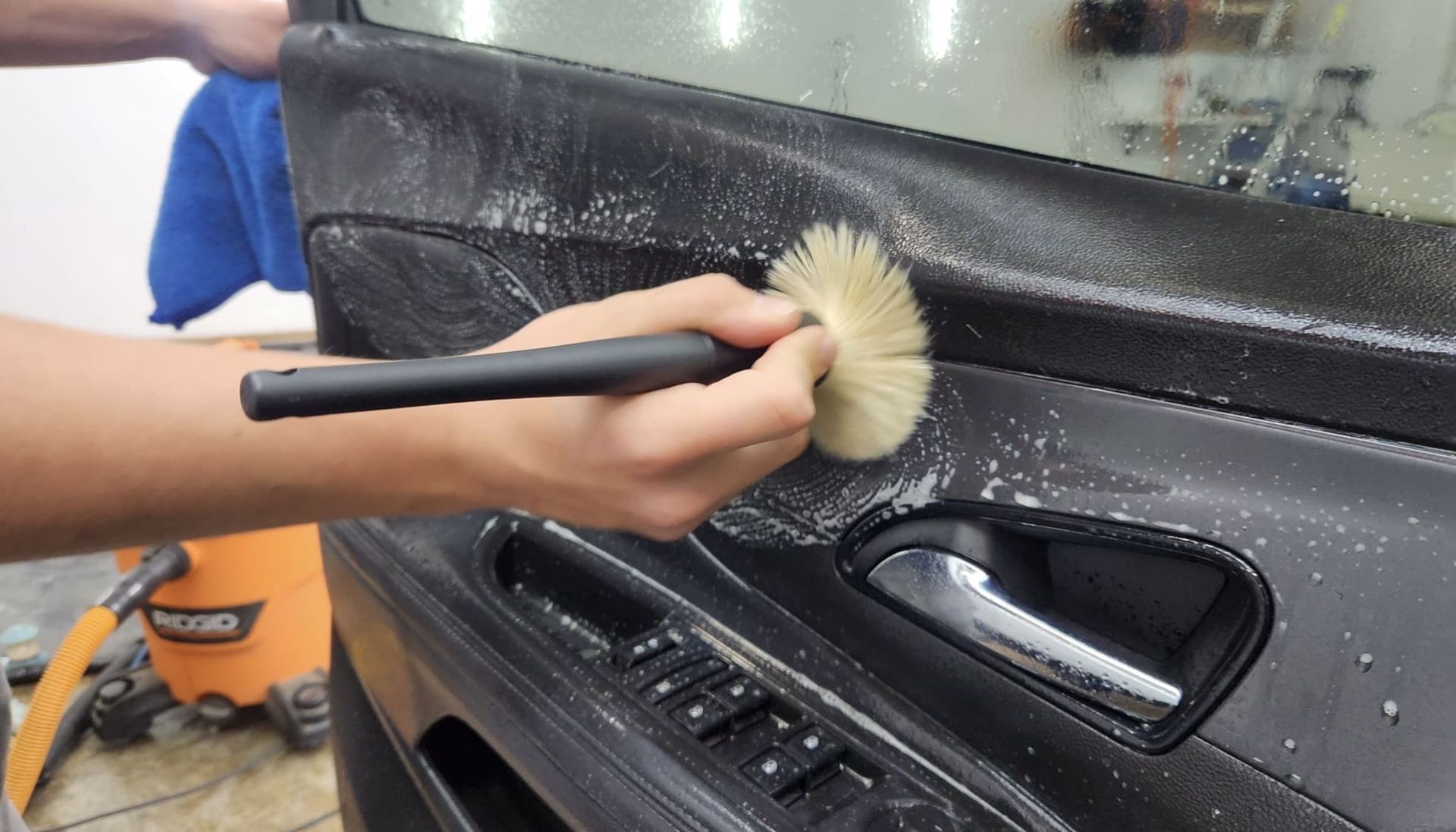 Hand cleaning car door panel with brush, suds visible.